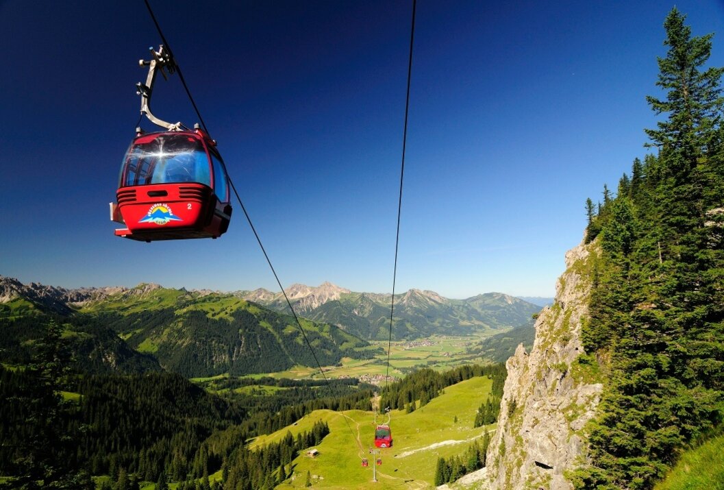 Rote Gondelbahn vor Berglandschaft mit grünen Wiesen und blauem Himmel