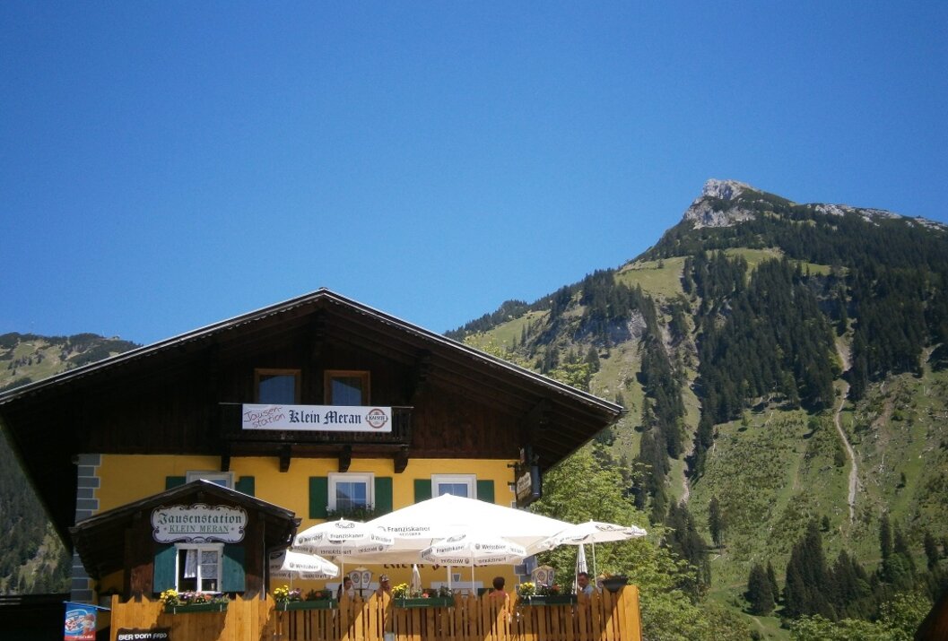 Gelbes Haus mit braunem Dach vor Bergkulisse unter blauem Himmel