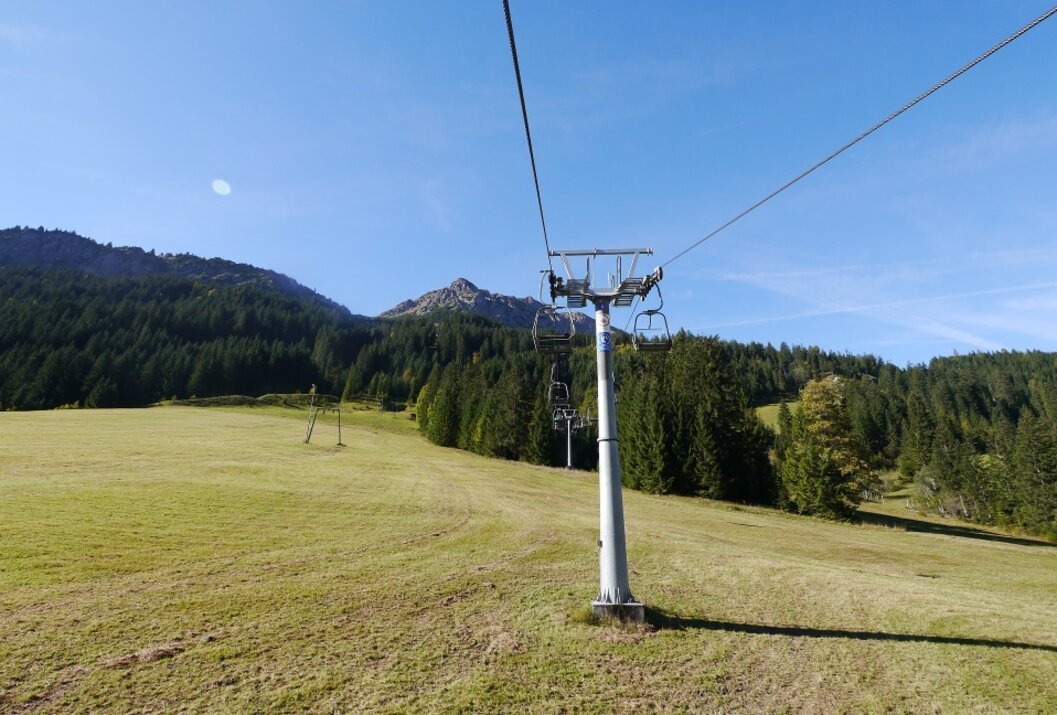 Sessellift über grüne Wiese mit Berg im Hintergrund an sonnigem Tag