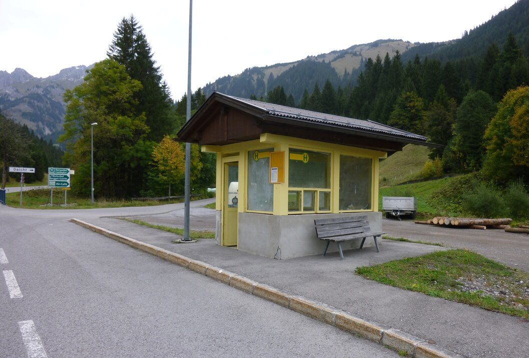 Gelbe Bushaltestelle mit Holzdach vor grüner Berglandschaft