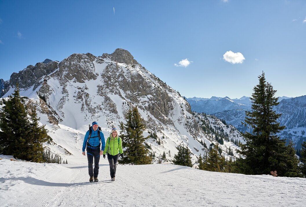Wanderpaar im Schnee vor Bergpanorama mit blauem Himmel
