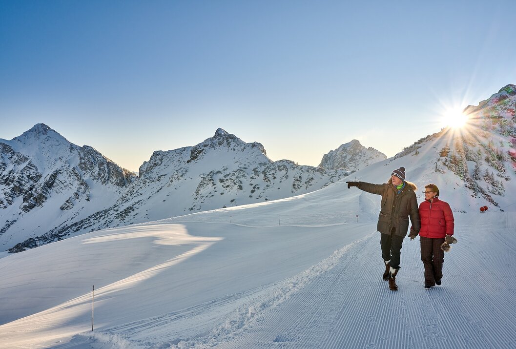 Zwei Personen wandern im Schnee, eine zeigt auf schneebedeckte Berge