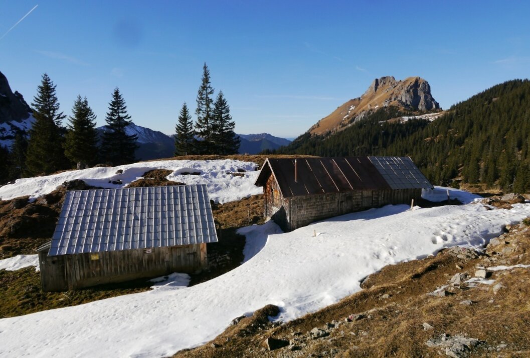 Almhütten im Schnee vor Berglandschaft unter blauem Himmel