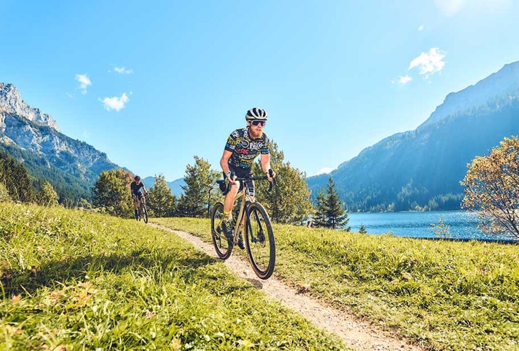 Radfahrer auf Schotterweg vor Bergpanorama und See