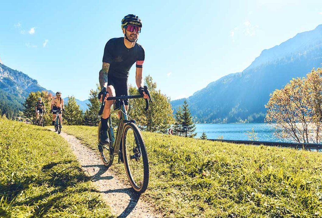 Radfahrer auf Schotterweg vor Bergsee, sonniger Tag