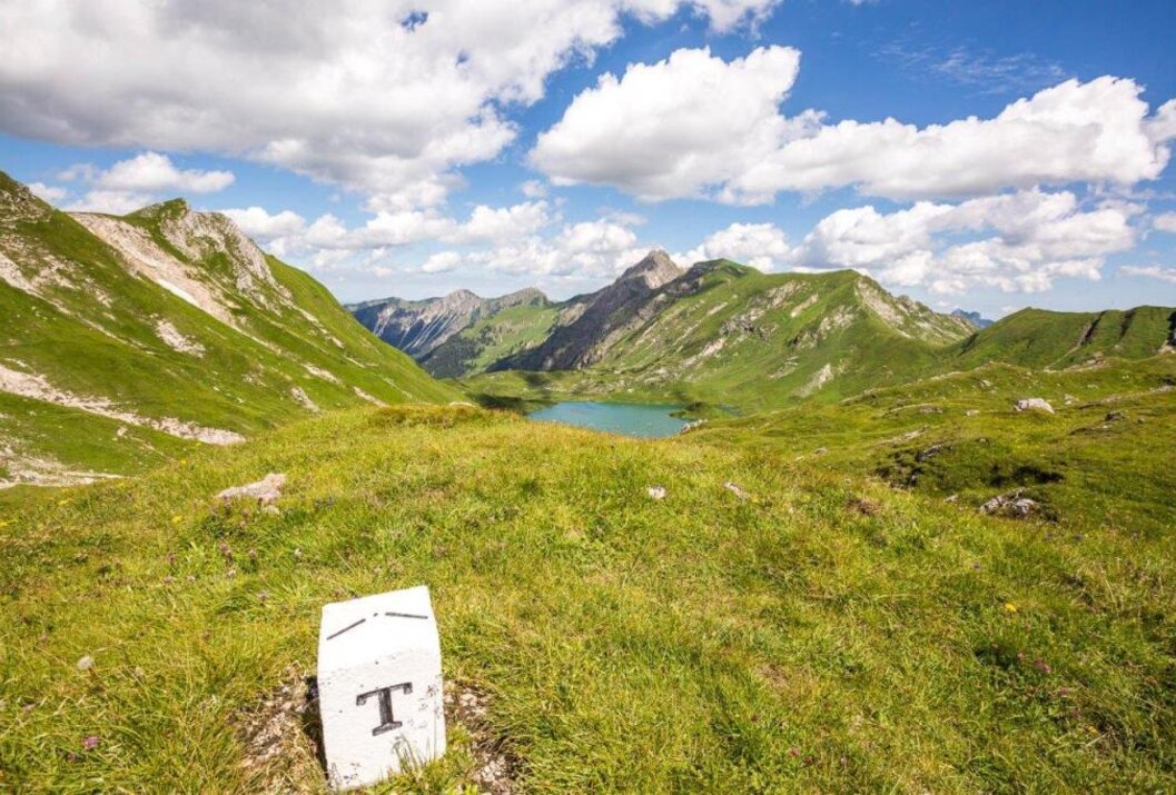 Berglandschaft mit See unter blauem Himmel mit Wolken und einem Grenzstein im Vordergrund
