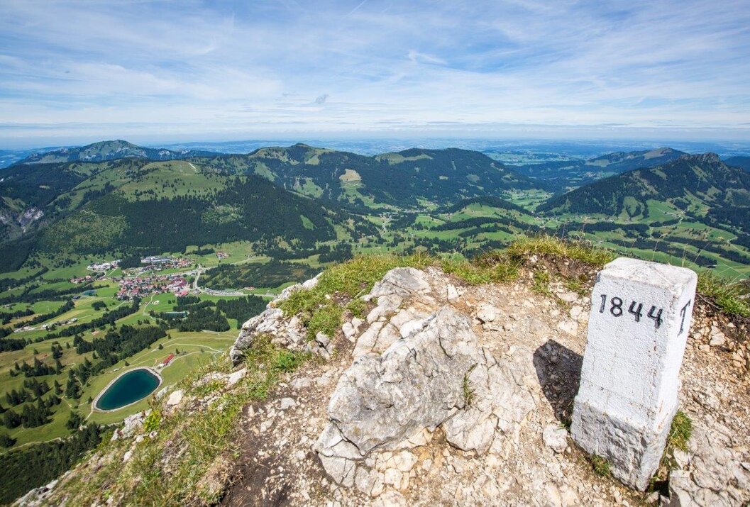 Berggipfel mit Blick auf grüne Landschaft und blauen Himmel