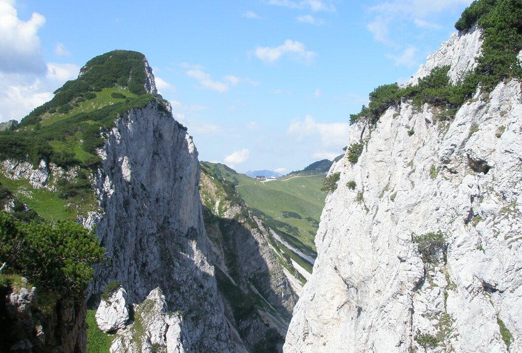 Berglandschaft mit steilen Felswänden und grünen Wiesen unter blauem Himmel