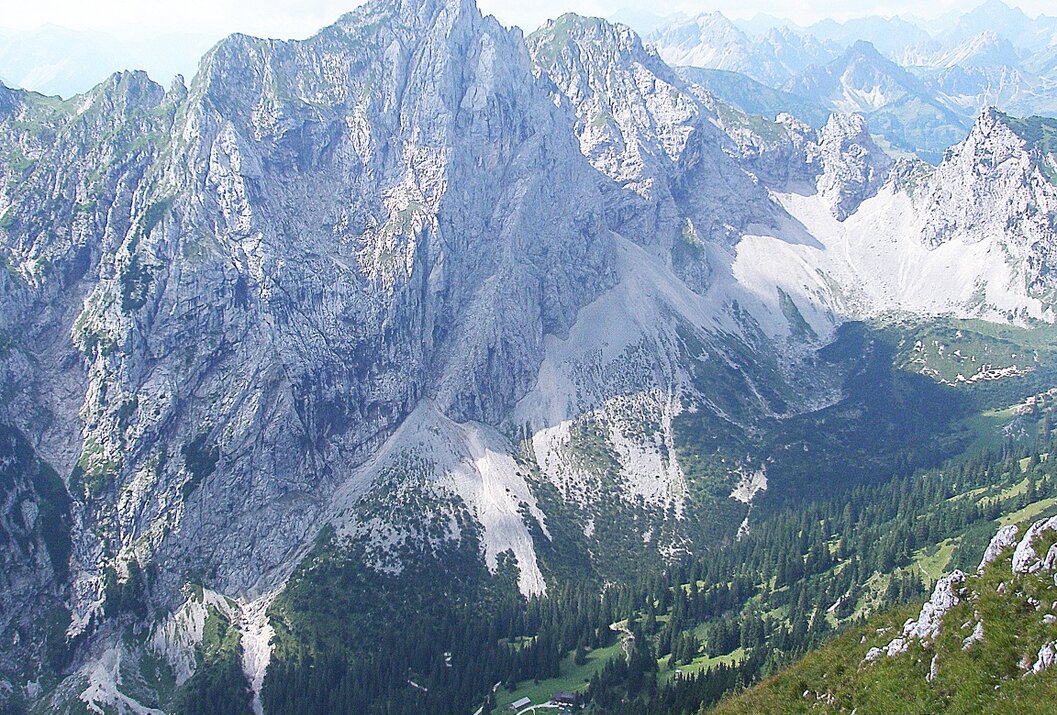 Berglandschaft mit steilen Felswänden und grünen Tälern unter bewölktem Himmel