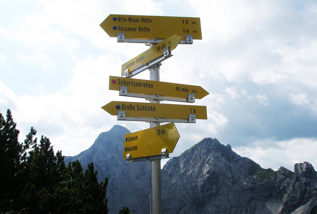 Gelber Wegweiser mit Wanderzielen vor Bergkulisse