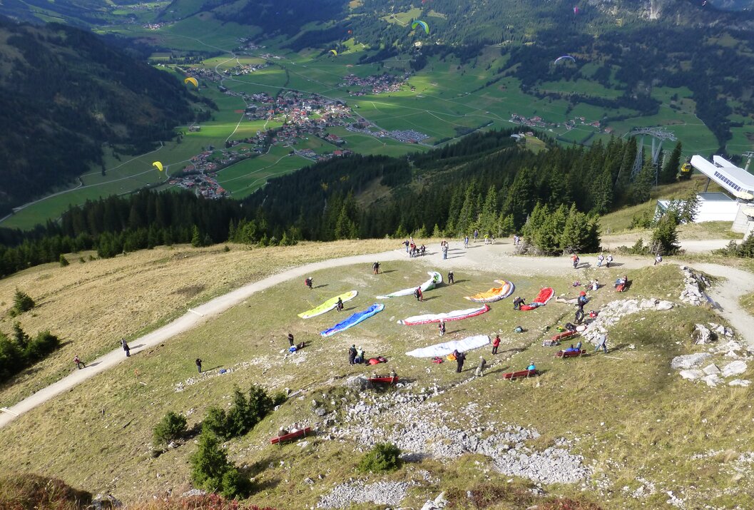 Paraglider bereiten sich auf einem Hügel zum Start vor, im Hintergrund grüne Landschaft