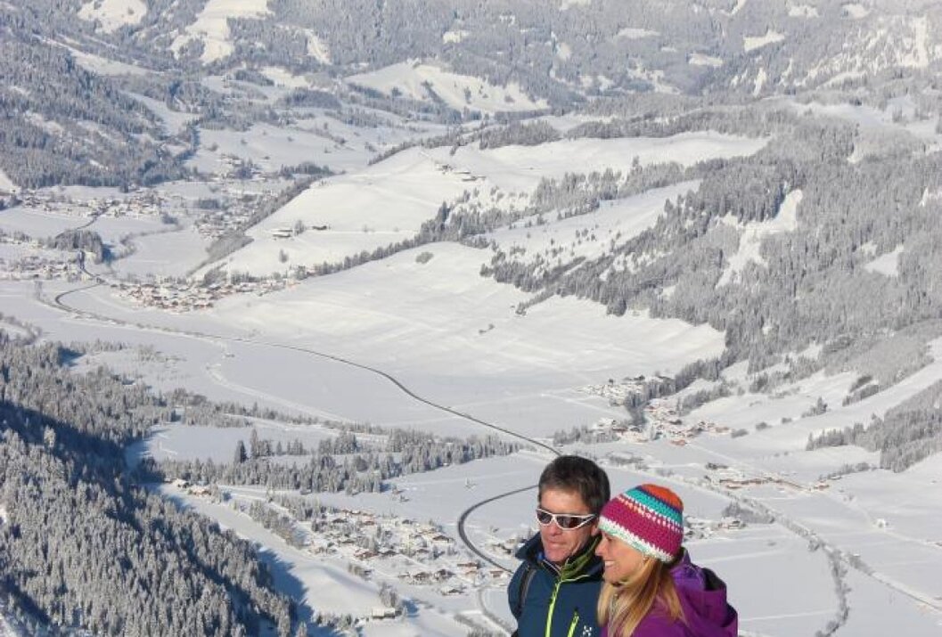 Paar vor verschneiter Berglandschaft mit Dörfern im Tal