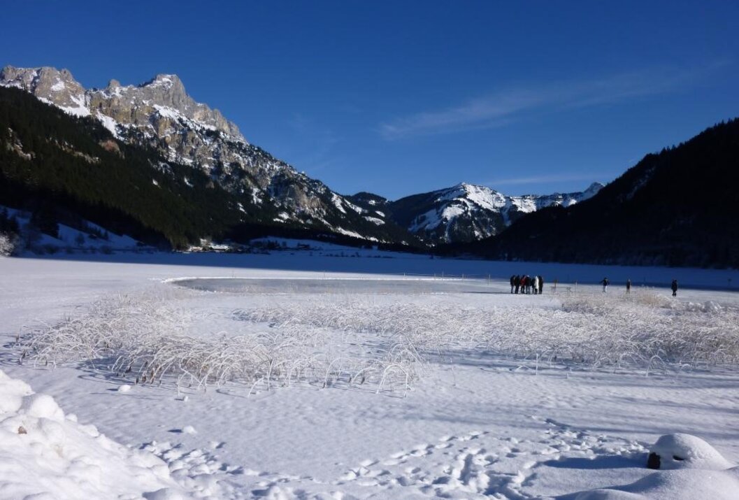 Verschneiter See mit Bergen im Hintergrund unter blauem Himmel