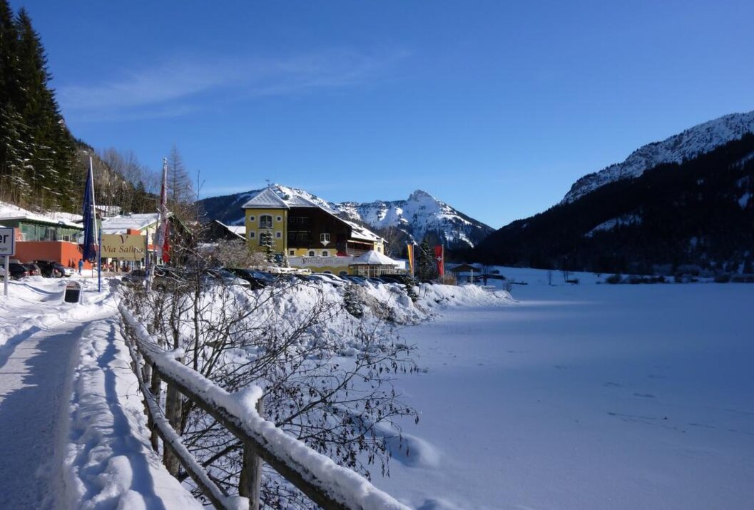 Winterliche Landschaft mit See, Häusern und Bergen unter blauem Himmel