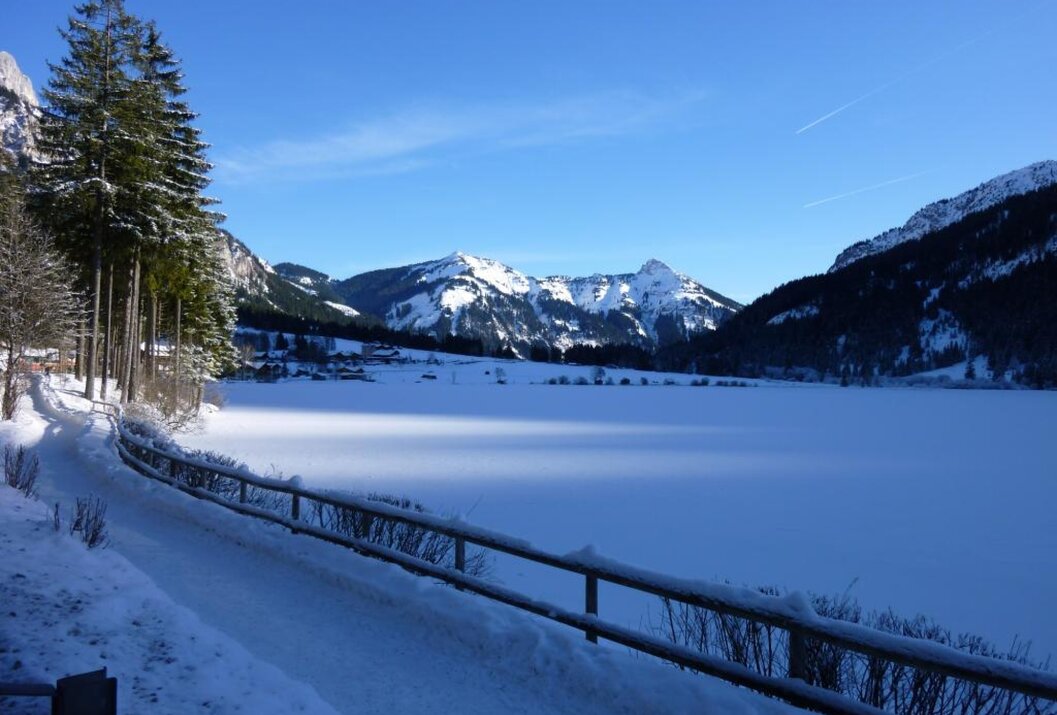 Winterlandschaft mit verschneitem See, Bergen und blauem Himmel