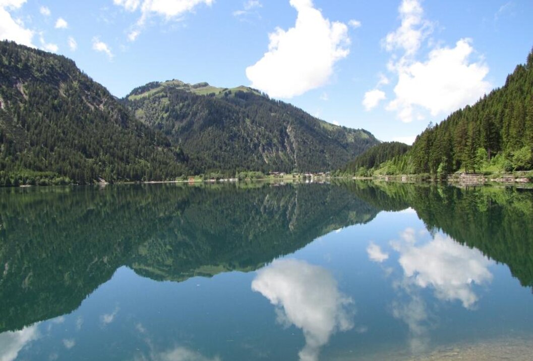 Bergsee mit Spiegelung von Bergen und Wolken im klaren Wasser