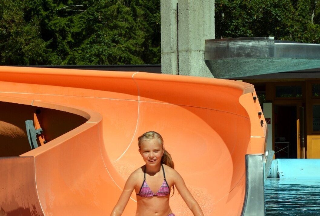 Mädchen in Bikini rutscht orangefarbene Wasserrutsche hinunter