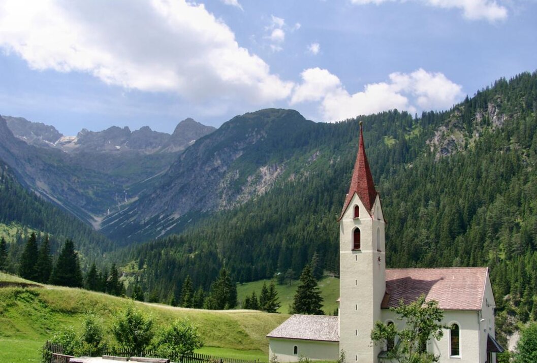Kirche mit rotem Dach vor Berglandschaft und blauem Himmel