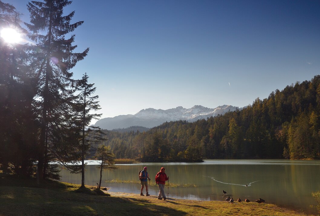 Zwei Wanderer am Seeufer, im Hintergrund Berge und Wald
