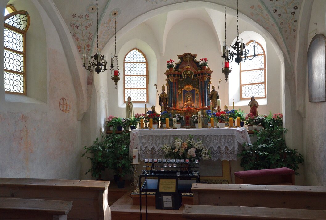 Innenansicht einer kleinen Kirche mit Altar, Heiligenfiguren und floraler Dekoration