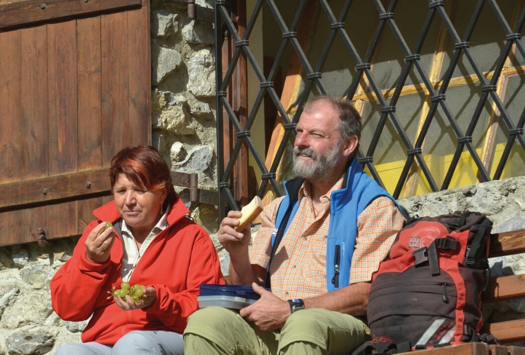 Wandererpaar rastet auf Bank vor Hütte und isst Proviant