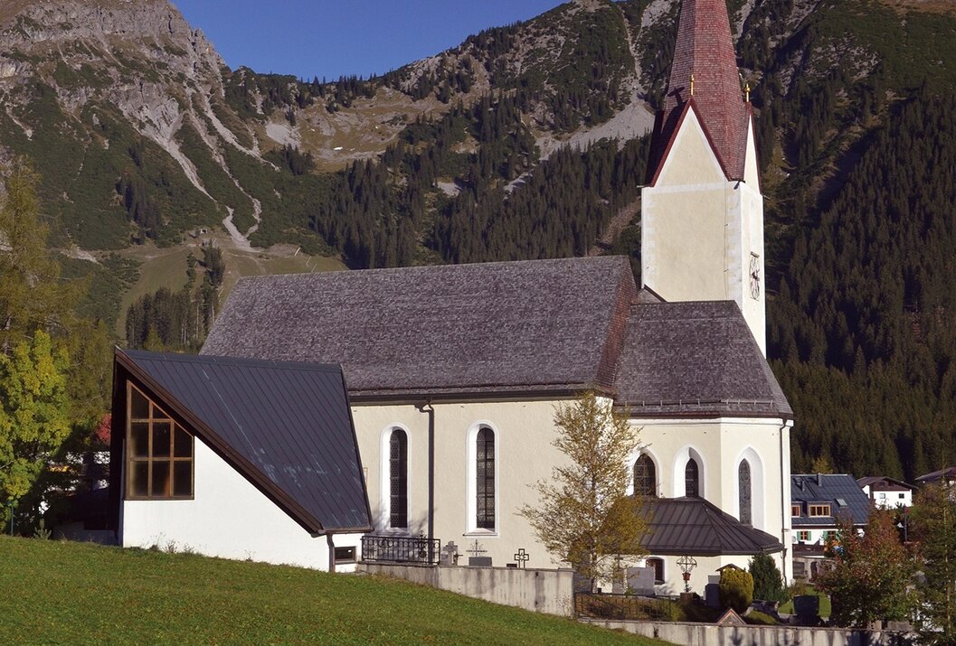Kirche mit rotem Turm vor Bergkulisse auf grüner Wiese