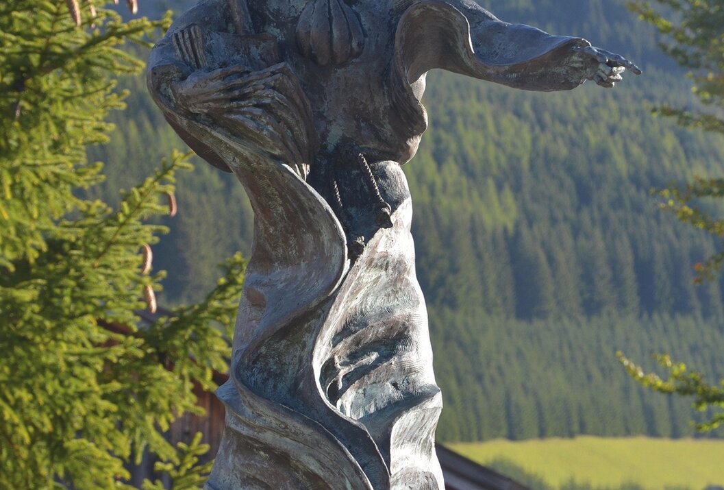 Bronzefarbene Statue eines Musikers mit Instrument vor Berglandschaft
