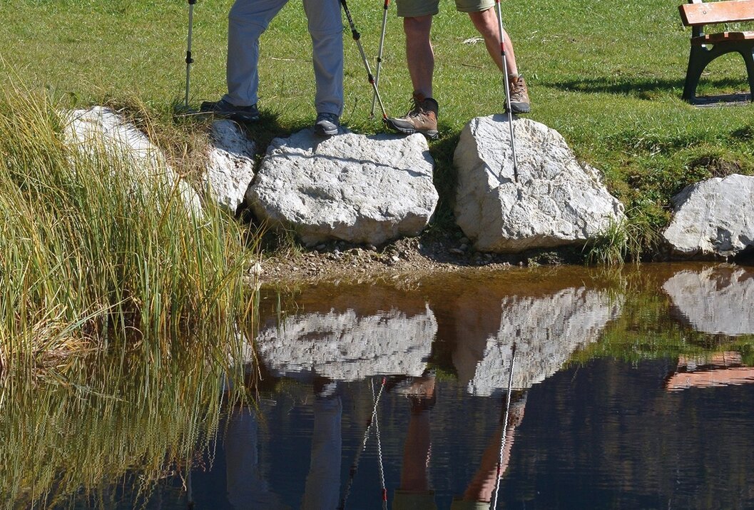 Zwei Wanderer mit Stöcken am See, Spiegelung im Wasser