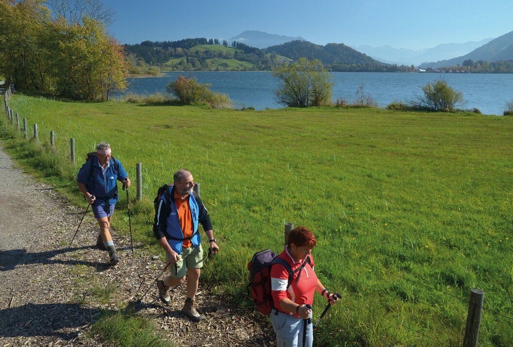 Wanderer auf Pfad mit See und Bergen im Hintergrund