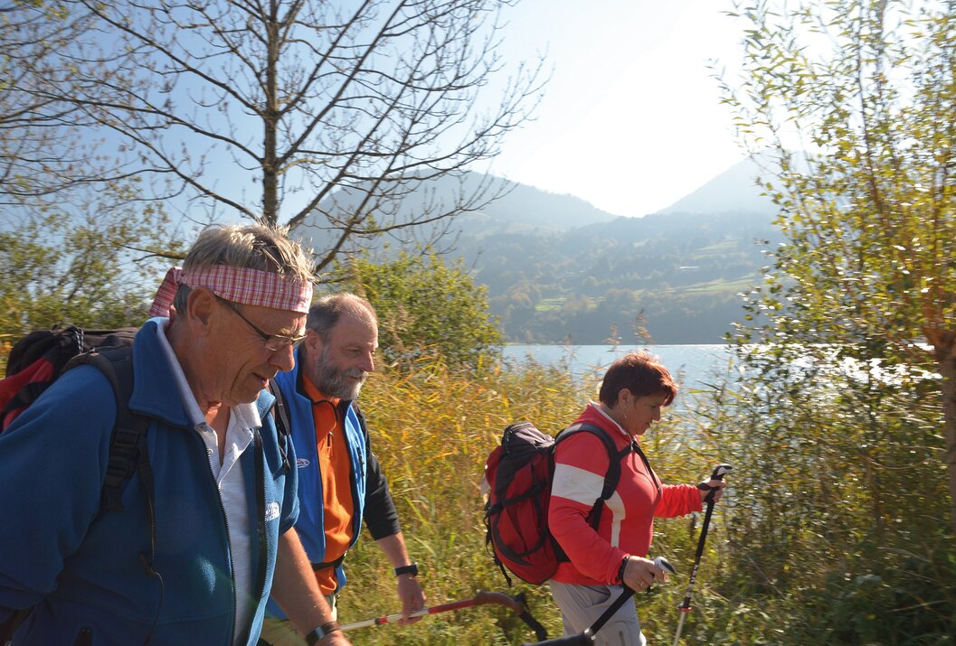 Wandergruppe mit Stöcken vor See und Bergen