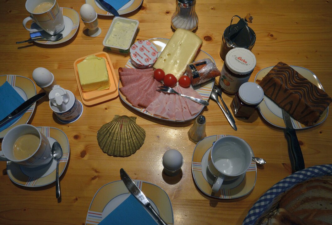 Gedeckter Frühstückstisch mit Wurst, Käse, Eiern, Marmelade, Butter und einer goldenen Muschel