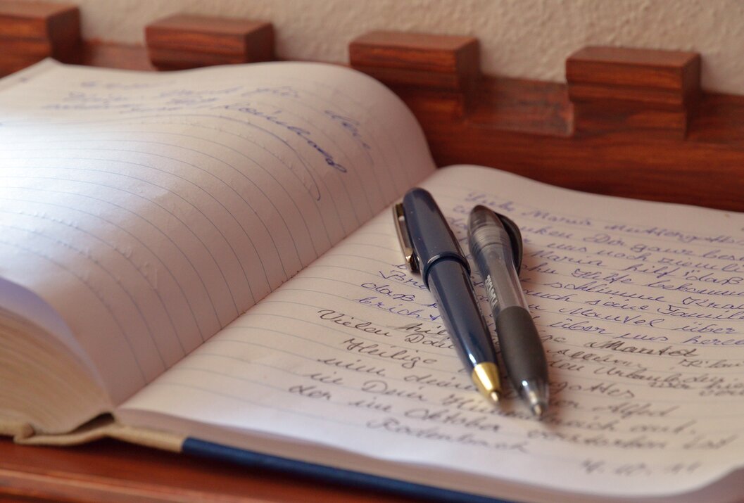 Offenes liniertes Notizbuch mit handschriftlichem Text und zwei Stiften darauf