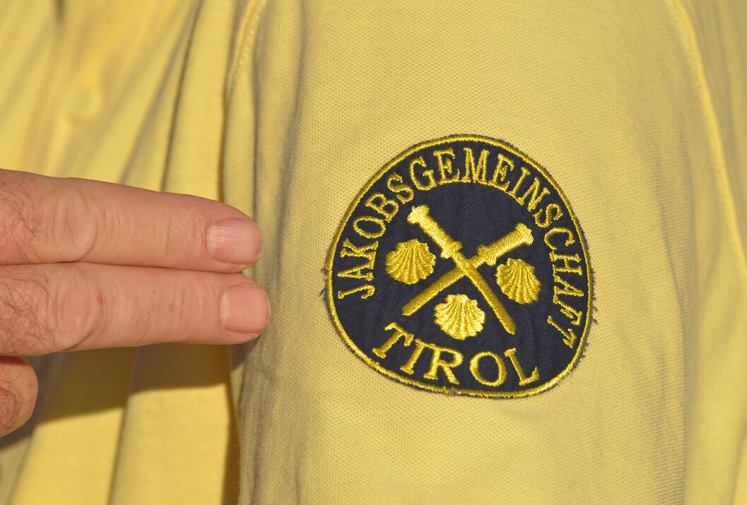 Gelbes Poloshirt mit aufgenähtem Logo Jakobsgesellschaft Tirol, Muscheln und gekreuzte Schwerter