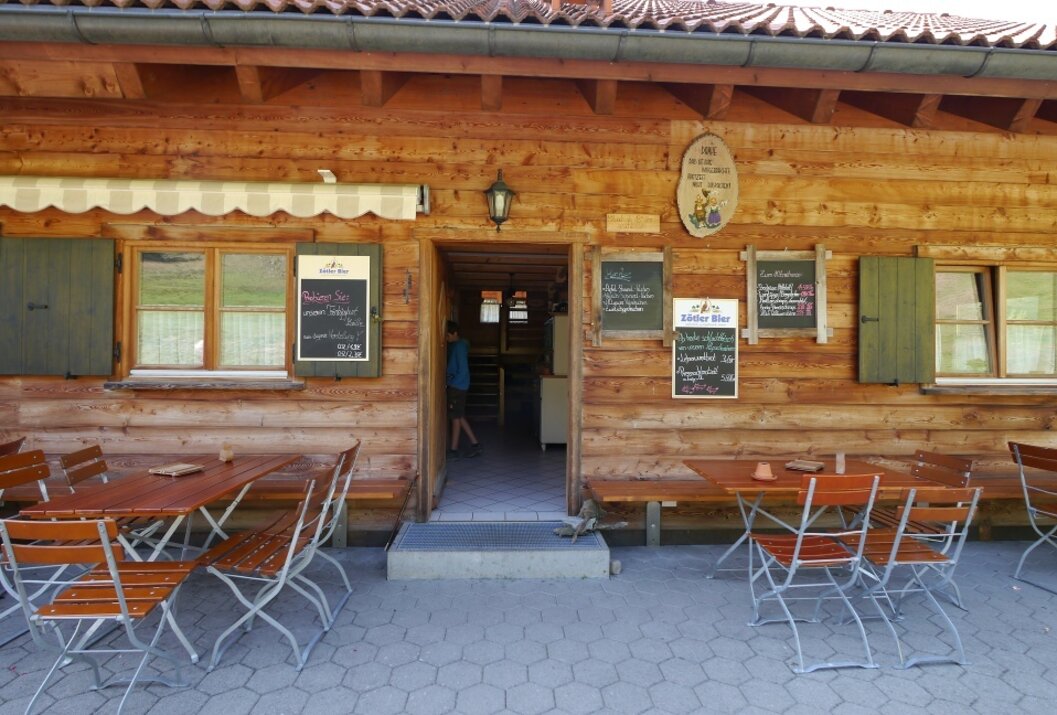 Hölzerne Hütte mit Tischen und Stühlen davor, Schilder mit Speisekarten hängen an der Wand