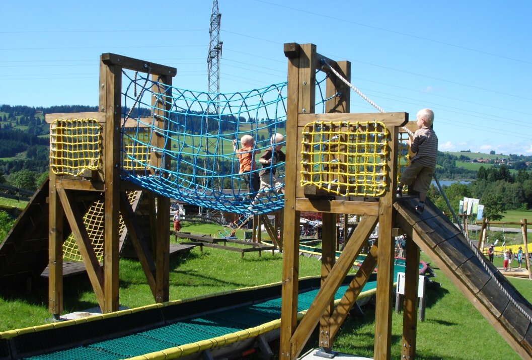 Kinder spielen auf einem hölzernen Spielplatz mit Netzbrücke und Rutsche im Freien