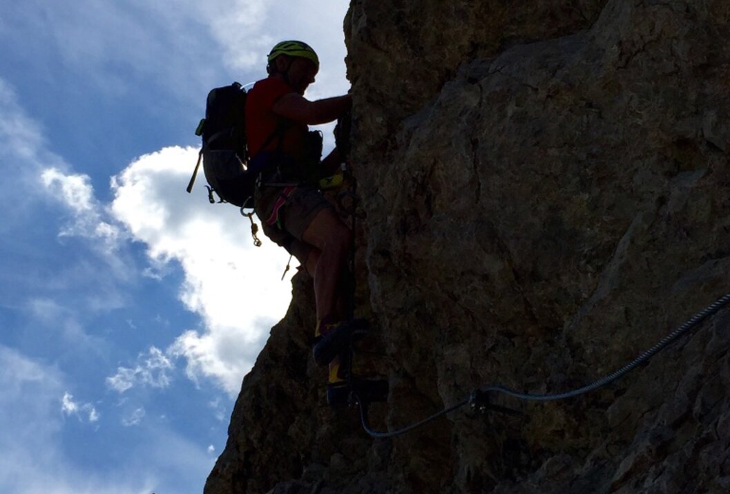 Kletterer am Felsen mit Seilversicherung vor blauem Himmel mit Wolken