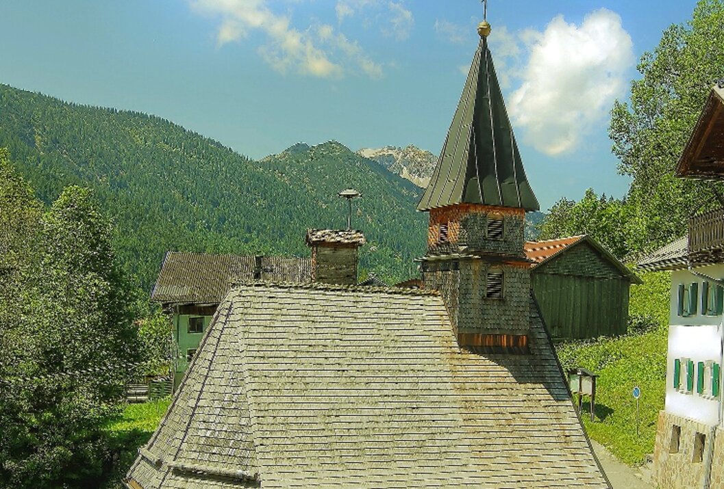 Kleine Kapelle mit Turm vor Berglandschaft und blauem Himmel