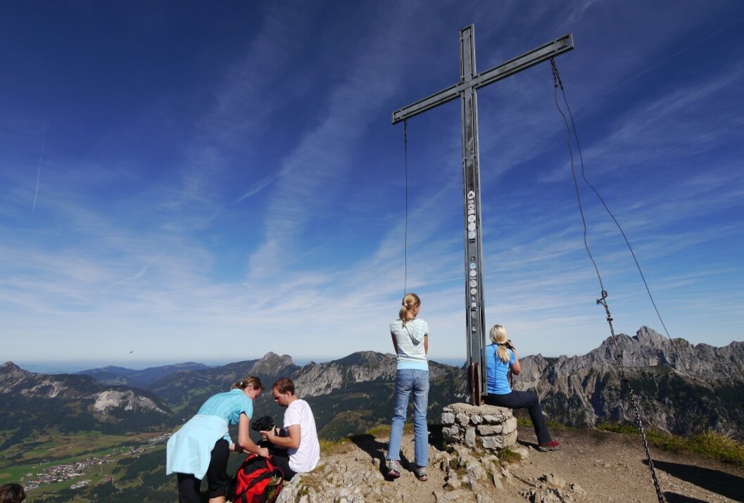 Menschengruppe am Gipfelkreuz mit Bergpanorama unter blauem Himmel