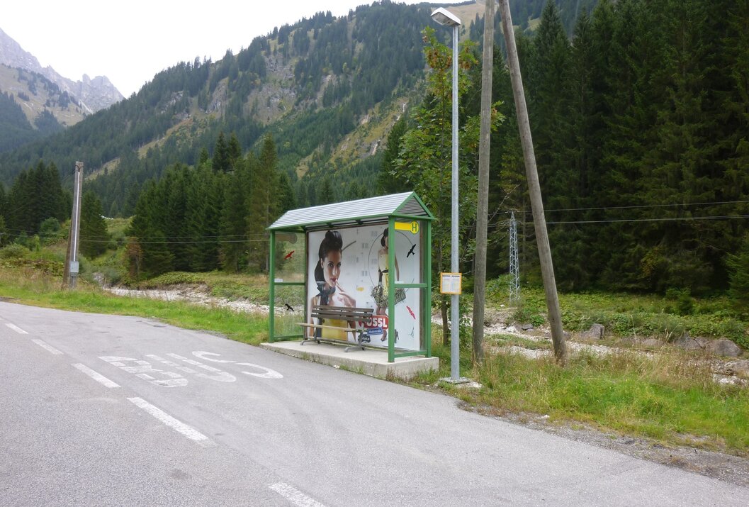 Bushaltestelle mit Werbeplakat vor Berglandschaft