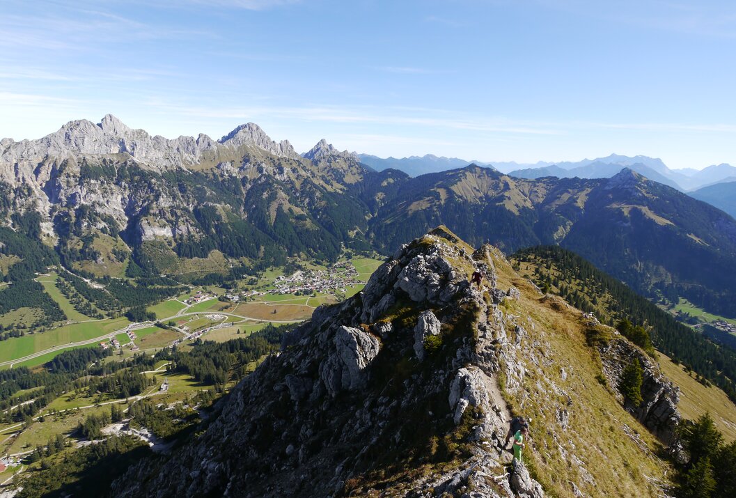 Bergkamm mit Wanderern, im Hintergrund grüne Täler und Bergkette unter blauem Himmel