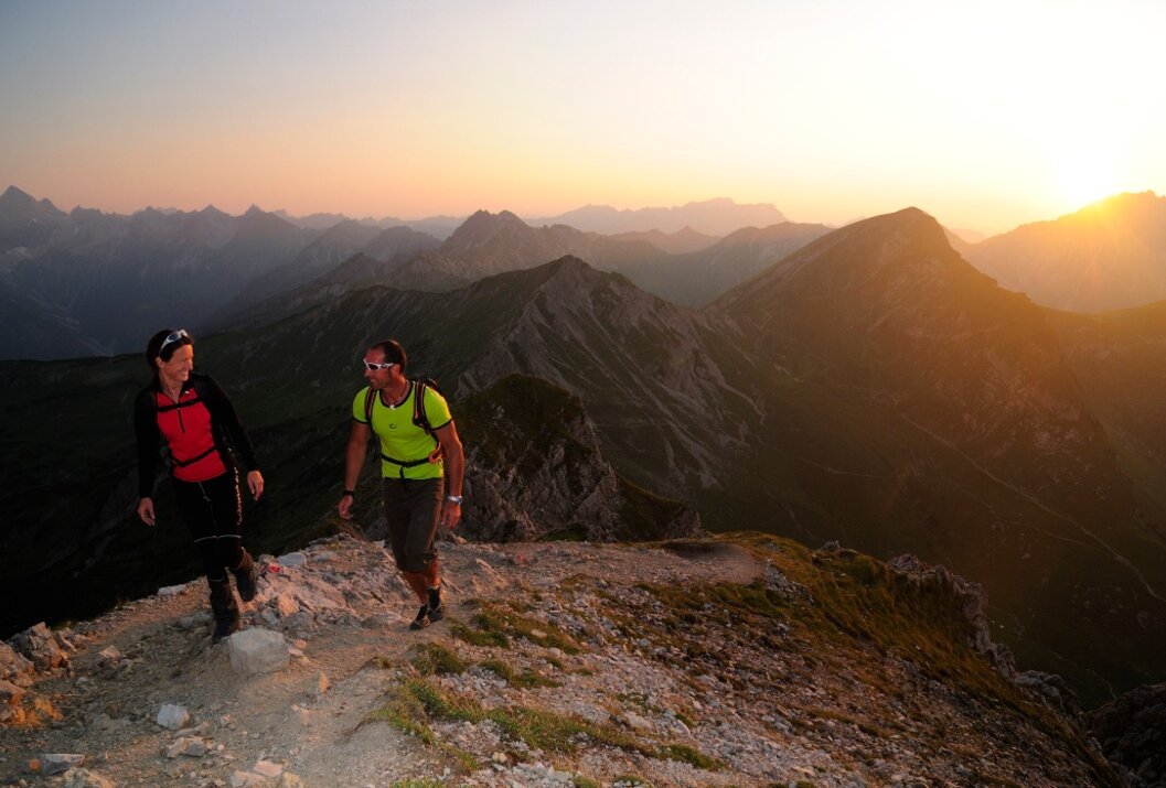 Zwei Wanderer auf einem Berggrat bei Sonnenaufgang mit Bergpanorama