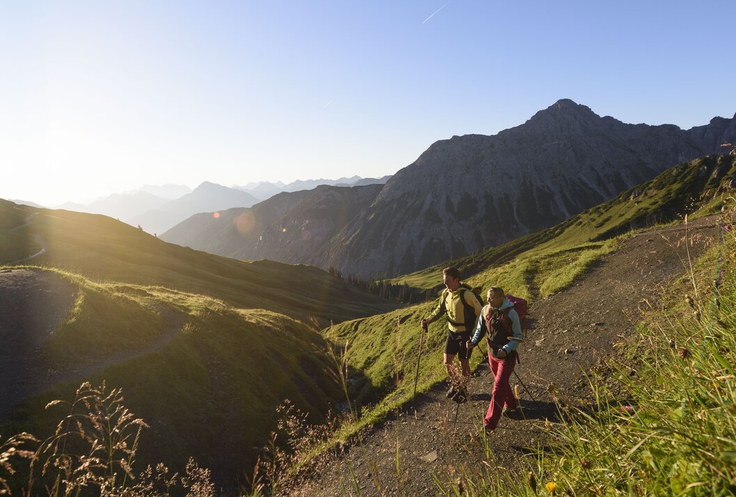 Wanderer auf Bergpfad mit Blick auf grüne Hügel und Gipfel im Sonnenlicht