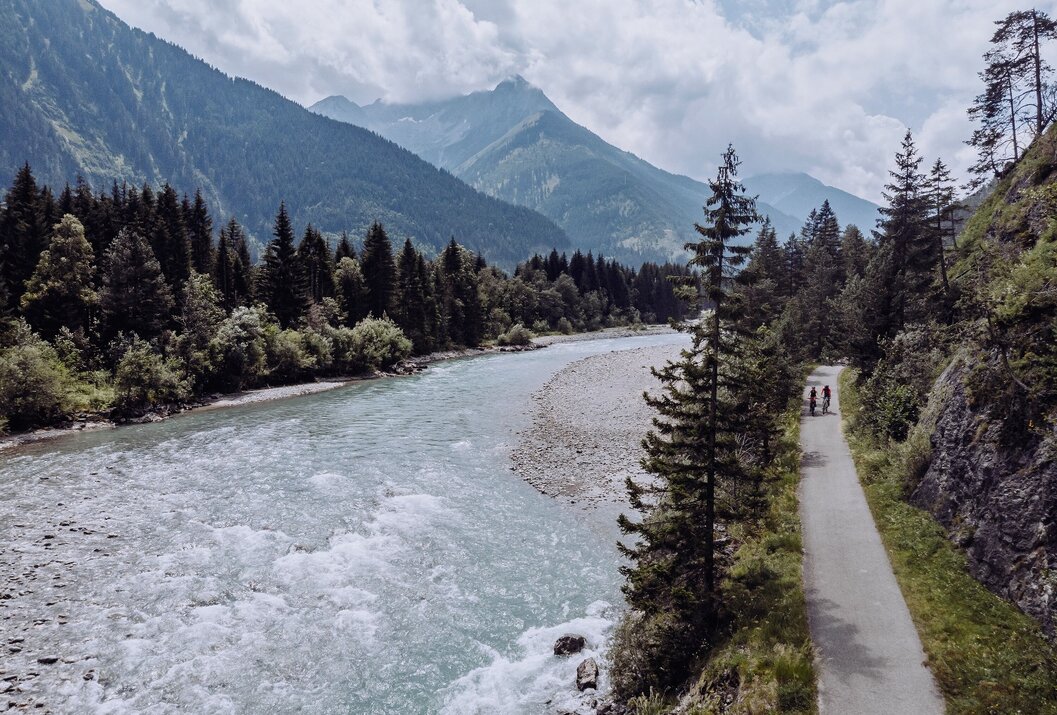 Fluss schlängelt sich durch grüne Landschaft, im Hintergrund Berge und bewölkter Himmel