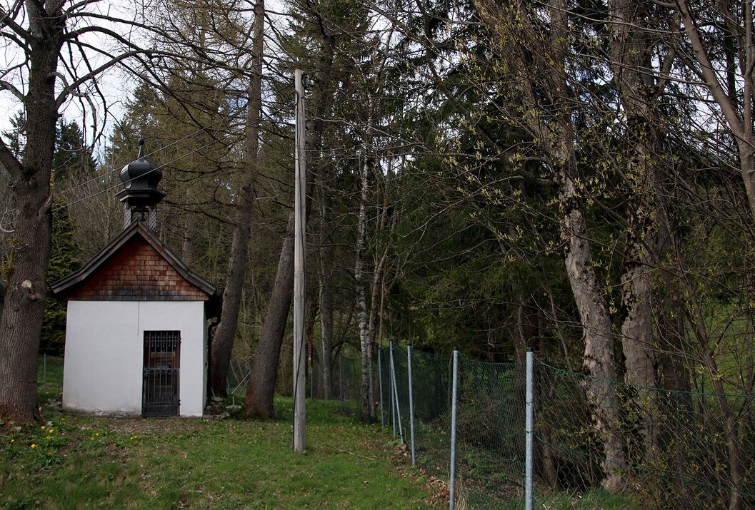Kleine Kapelle am Waldrand mit Zaun und Strommast