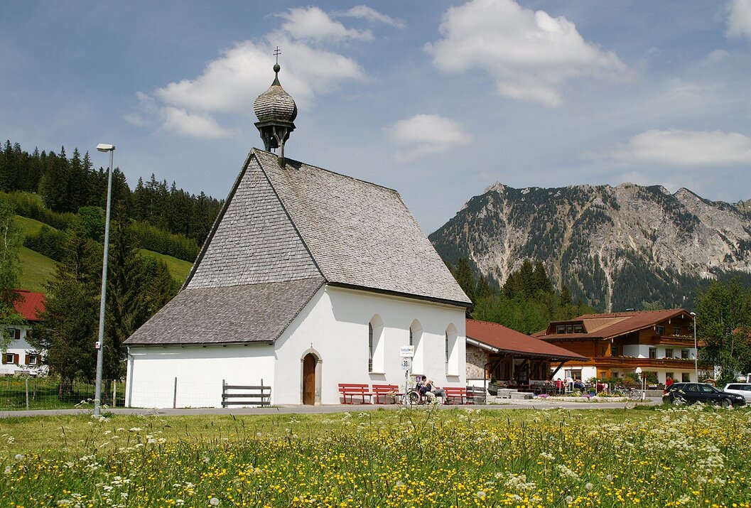 Kleine weiße Kirche auf grüner Wiese vor Bergkulisse