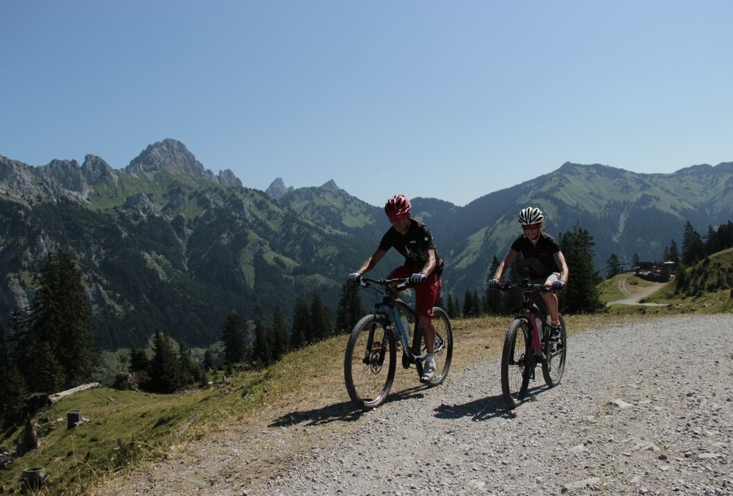 Zwei Mountainbiker fahren auf Schotterweg vor Bergkulisse