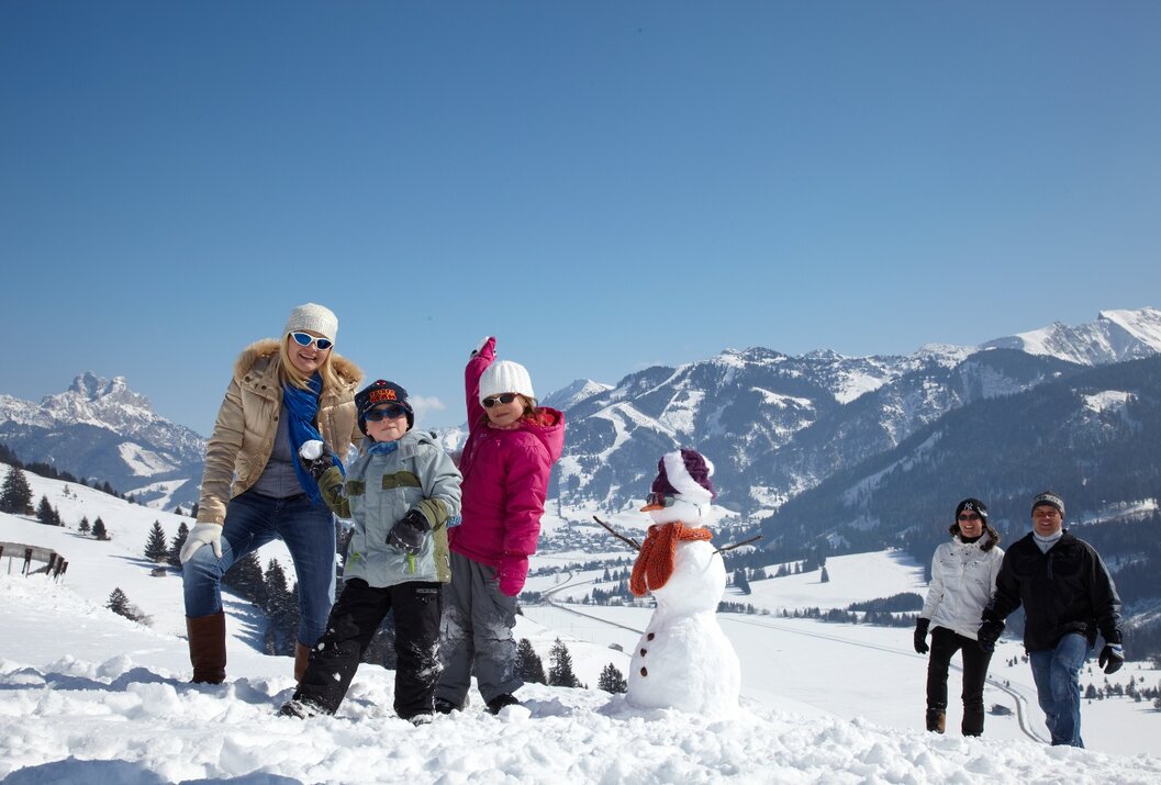 Familie baut Schneemann vor Bergpanorama an sonnigem Wintertag
