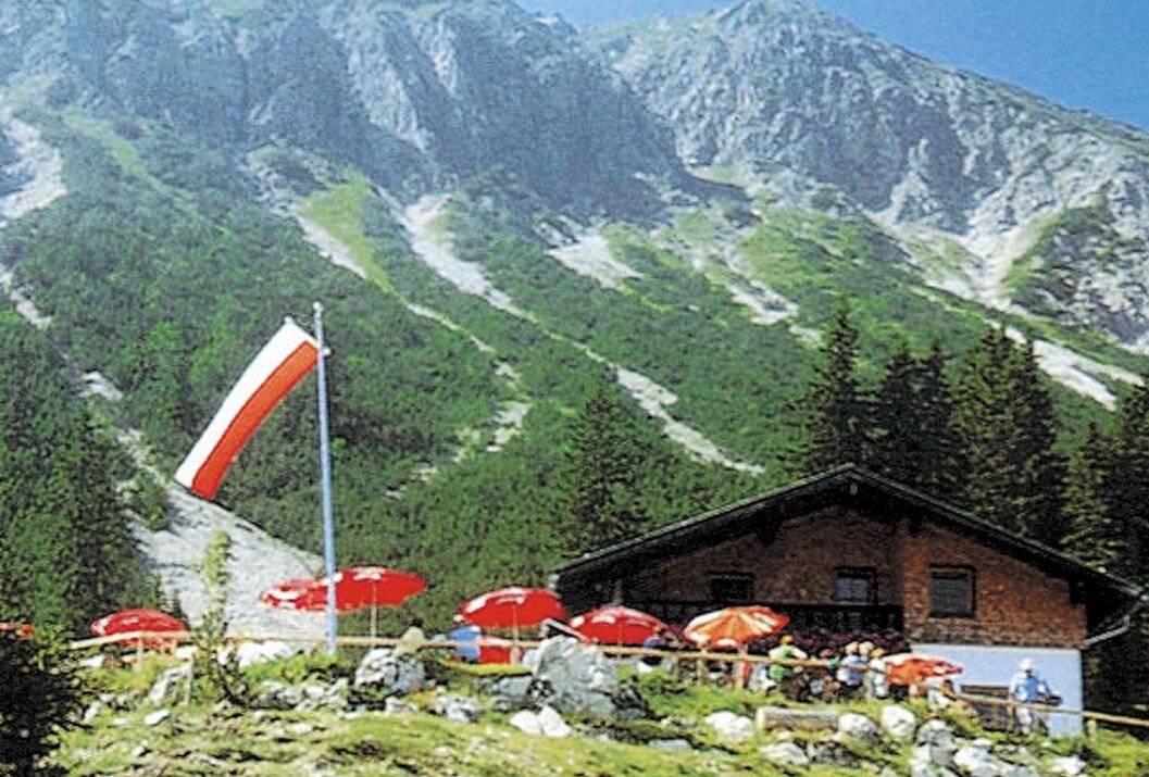Berghütte mit Terrasse vor Bergpanorama und rot-weiß gestreifter Fahne