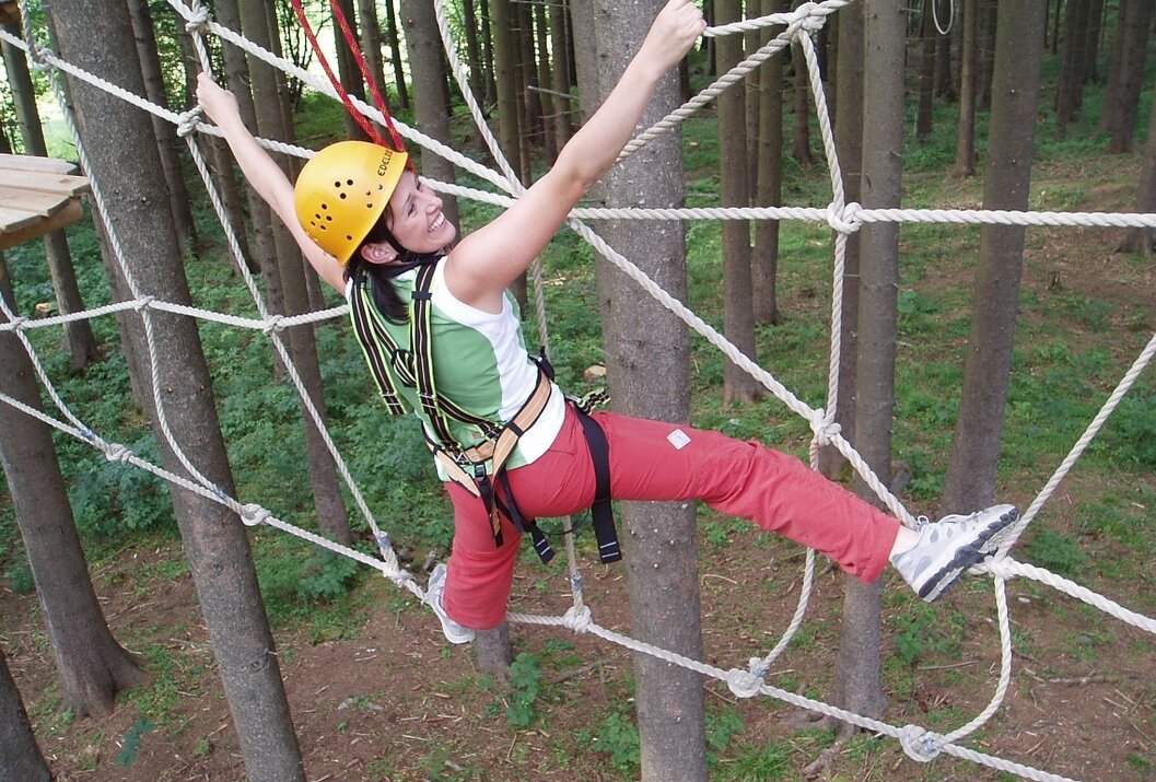 Frau mit Helm klettert in einem Hochseilgarten an einem Netz