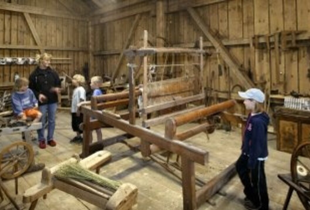 Webstuhl in einer Holzhütte, Kinder schauen zu